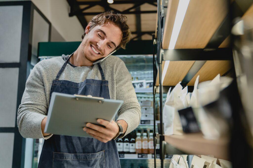 Smiling busy bartender checking goods while talking on phone in small cafeteria